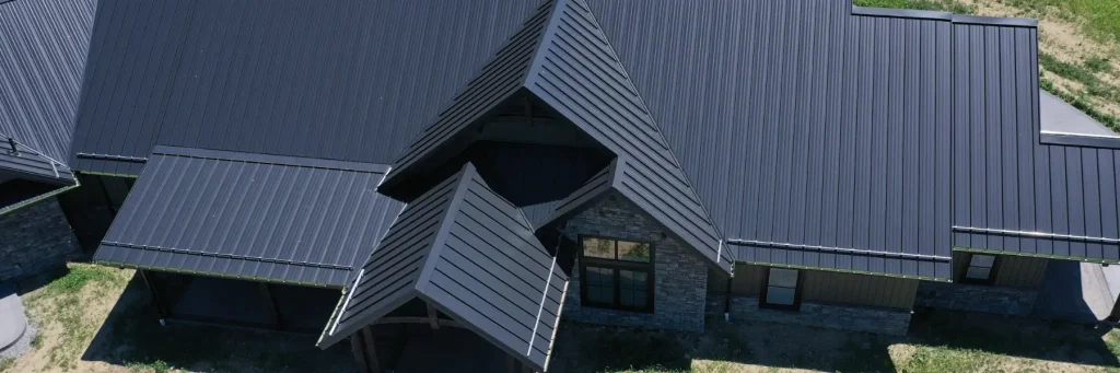 Aerial view of a modern house with a large and black metal roof featuring multiple peaks and angles