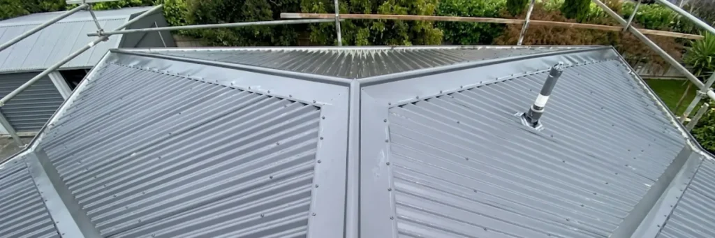 Metal roof with corrugated panels and a central seam is surrounded by scaffolding