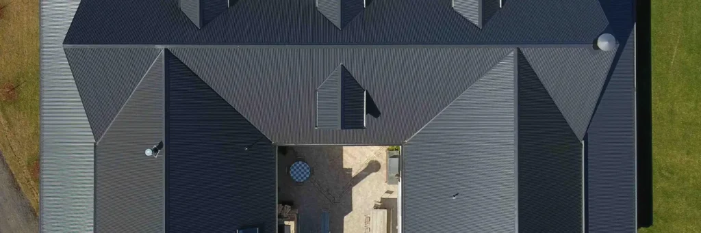 Aerial view of a large, dark gray metal-roofed building with multiple ridges