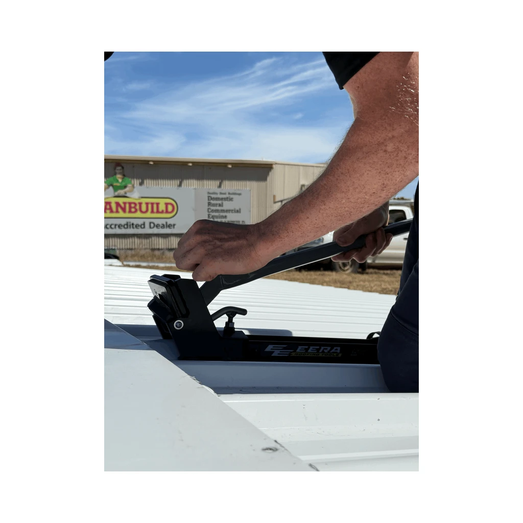 Hand on an EERA ridge cap notcher sitting on a white trapezoidal metal roof